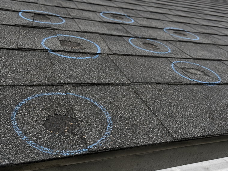 Hail impacts on an asphalt shingle roof marked with blue chalk circles during a storm damage inspection